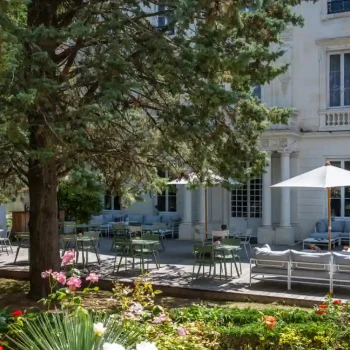 Jardin verdoyant et terrasse ombragée de l’Hôtel Le Champlain à La Rochelle, avec sculptures et mobilier d’extérieur élégant